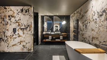 A modern bathroom with marble walls, a freestanding bathtub, and a double sink vanity.
