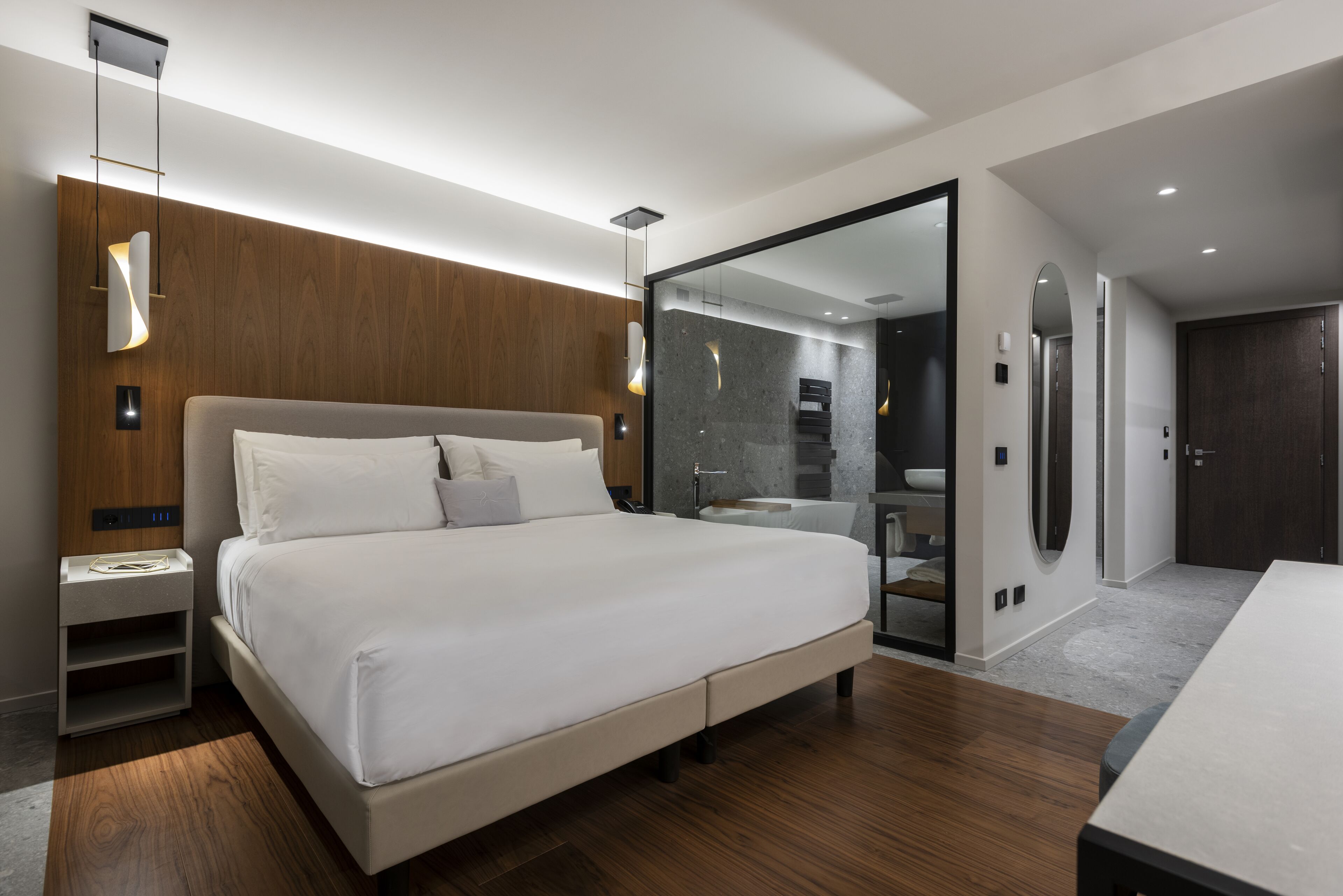 Un dormitorio moderno con una cama grande, mesitas de noche, un espejo y un vestidor.
