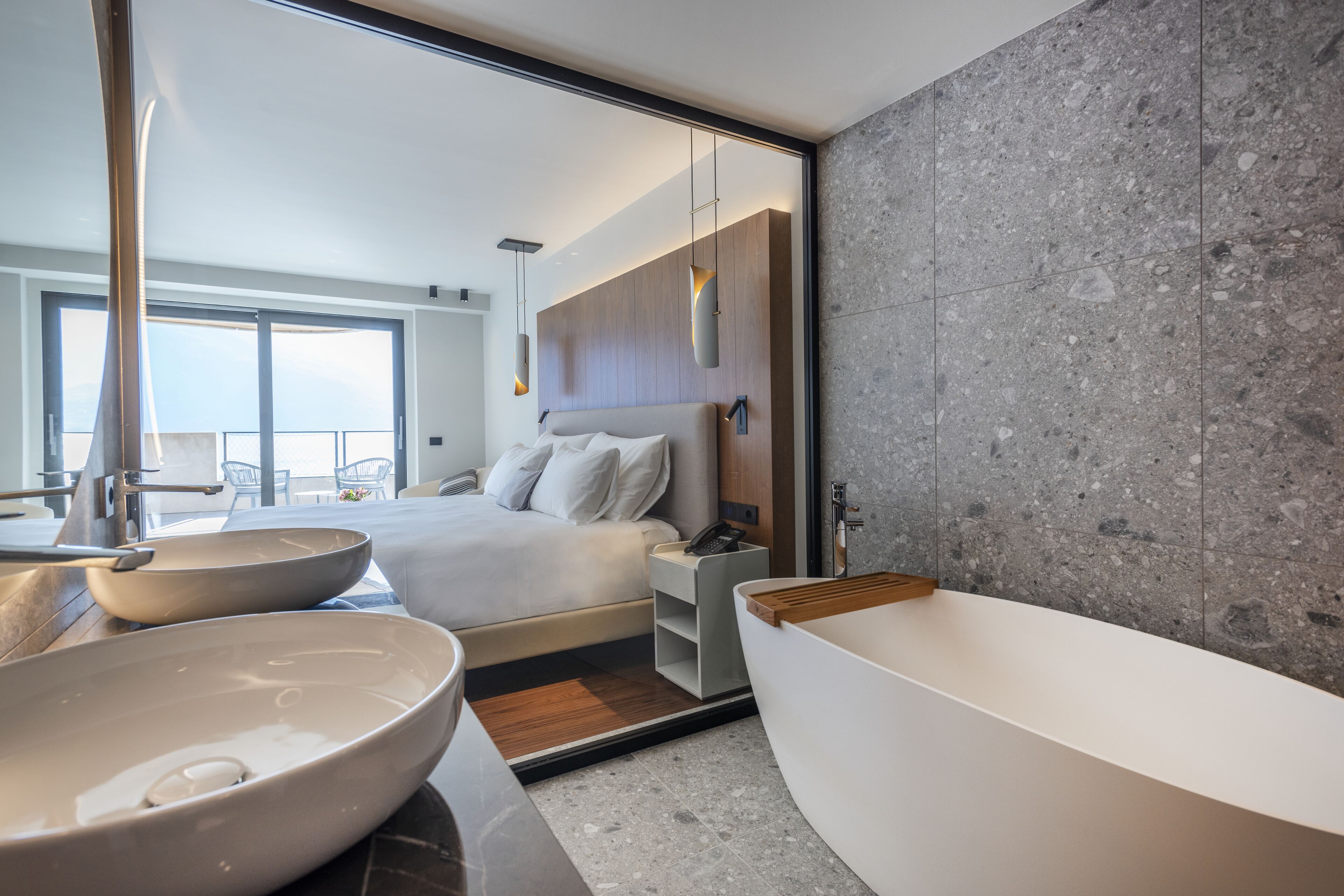 A modern bathroom with a large bathtub, two bowls, a bed with a view, and a large mirror.