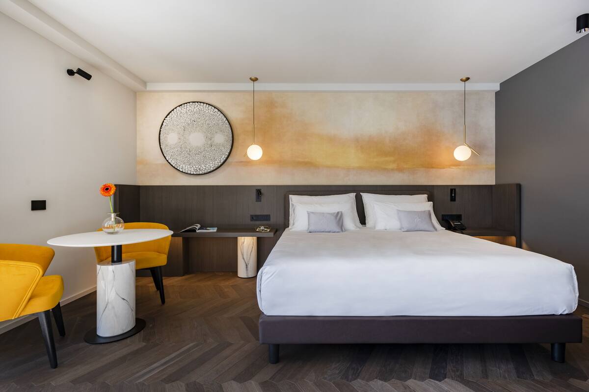Una habitación de hotel moderna con una cama grande, una mesa redonda con sillas y una obra de arte colgada en la pared.