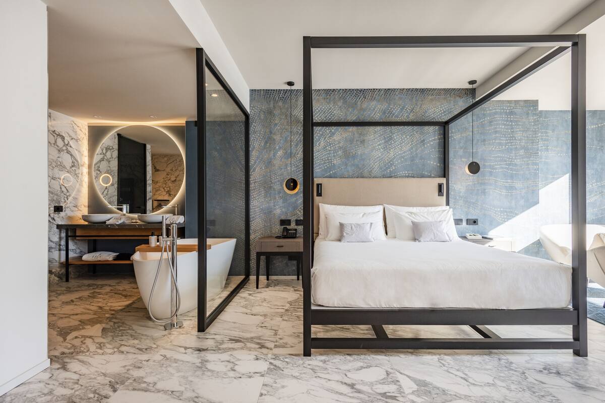 Una habitación de hotel moderna con una cama grande, un baño con bañera y suelo de mármol.