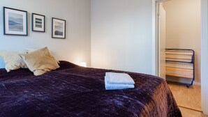 Ein Schlafzimmer mit dunkelblau gesteppter Bettdecke, zwei Kissen und drei gerahmten Bildern an der Wand.