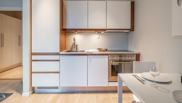 Eine kleine Küche mit weißen Schränken, einem eingebauten Backofen und einem Essbereich mit Tisch und Stühlen.