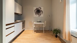 Eine kleine Küche mit weißen Schränken, einem Esstisch mit zwei Stühlen, einem Topf mit Pflanze und einem großen Blumenbild an der Wand.