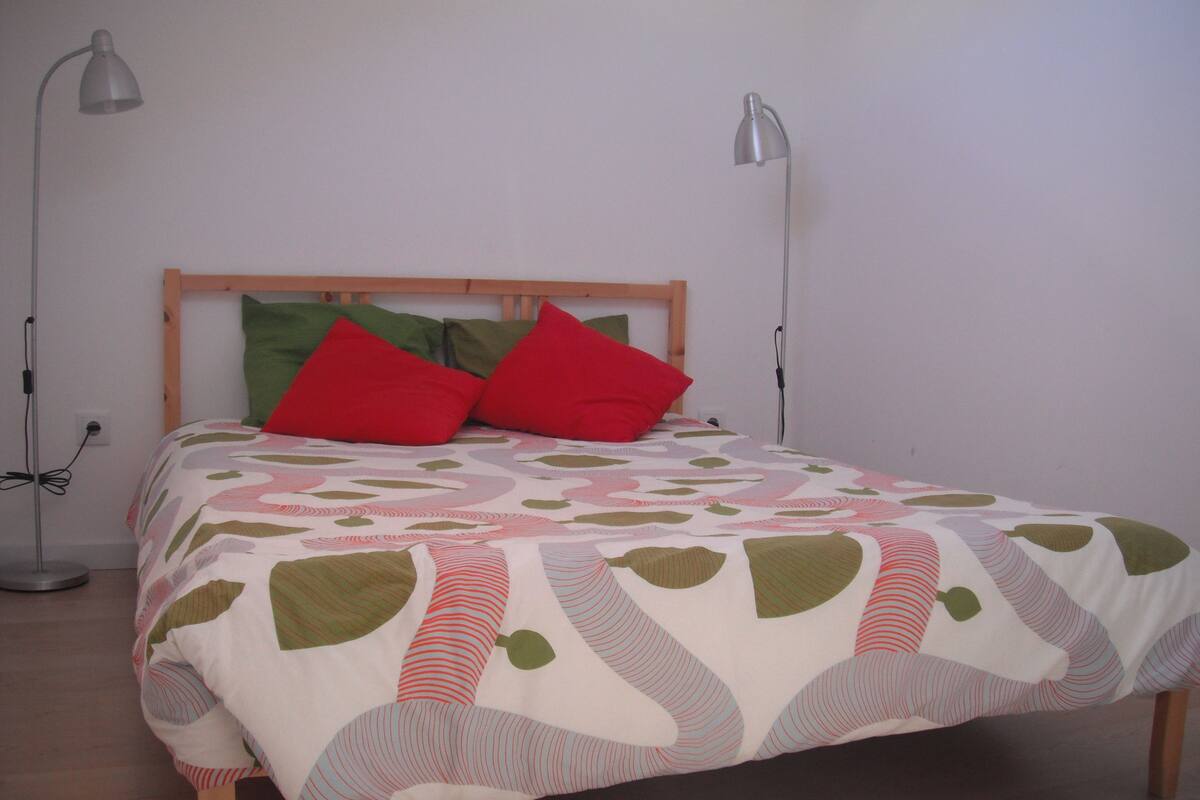A bed with a patterned bedspread, two red pillows, and a wooden headboard.