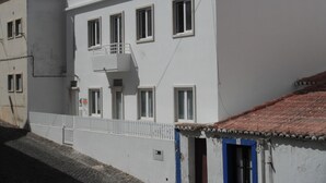 A white building with a red-tiled roof, a balcony, and a blue door. - 70's Hostel (Mafra)