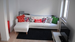 A modern living room with a white sofa, black rug, and a flat-screen TV on a white stand. - 70's Hostel (Mafra)
