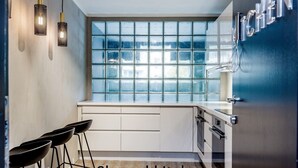 A modern kitchen with a large window, white cabinetry, and a bar stool area. - New Studio Prime Location (Oslo)