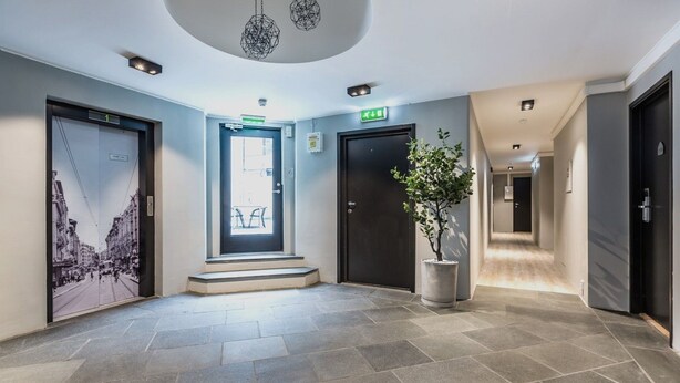 A modern hotel lobby with a large entrance door, a staircase leading to the upper floor, a potted plant, and a hallway with doors. - New Studio Prime Location (Oslo)