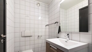 A modern bathroom with white tiles, a white sink, a mirror, and a toilet. - New Studio Prime Location (Oslo)