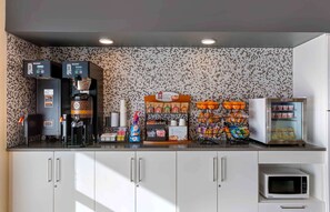 A kitchenette with a coffee machine, a microwave, and a refrigerator. There are shelves with snacks and a basket of oranges. - Extended Stay America Premier Suites Phoenix Chandler Downto (Chandler)
