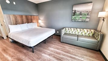 Una habitación de hotel con cama, sofá, lámpara de pared y un cuadro.