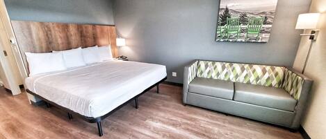A hotel room with a bed, a sofa, a wall-mounted lamp, and a painting.