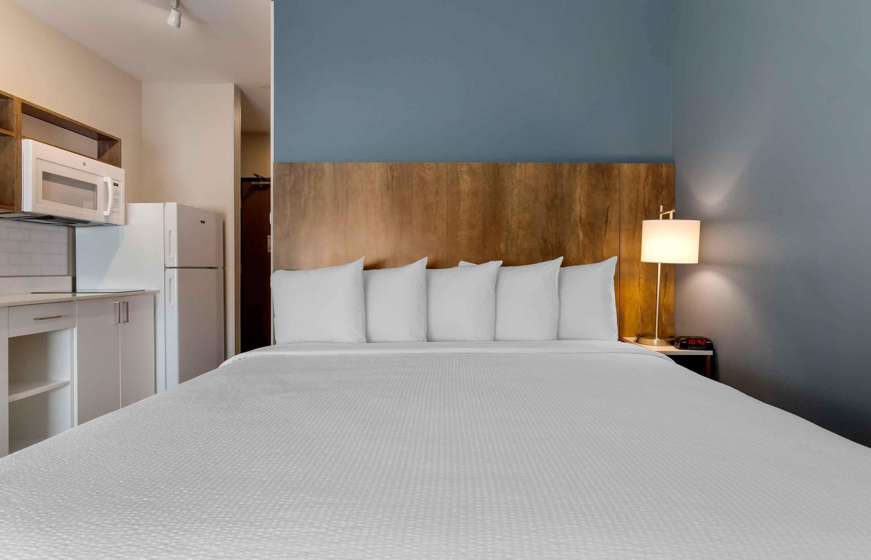 A hotel room with a bed, a nightstand with a lamp, a microwave, and a refrigerator.