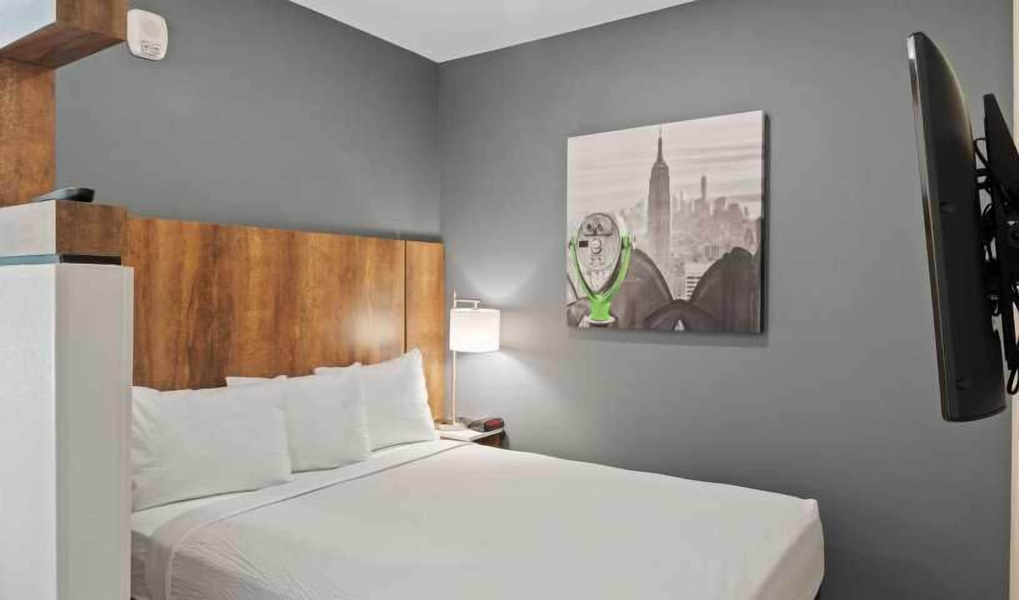 A hotel room with a bed, a wooden headboard, a nightstand with a lamp, and a wall-mounted television.