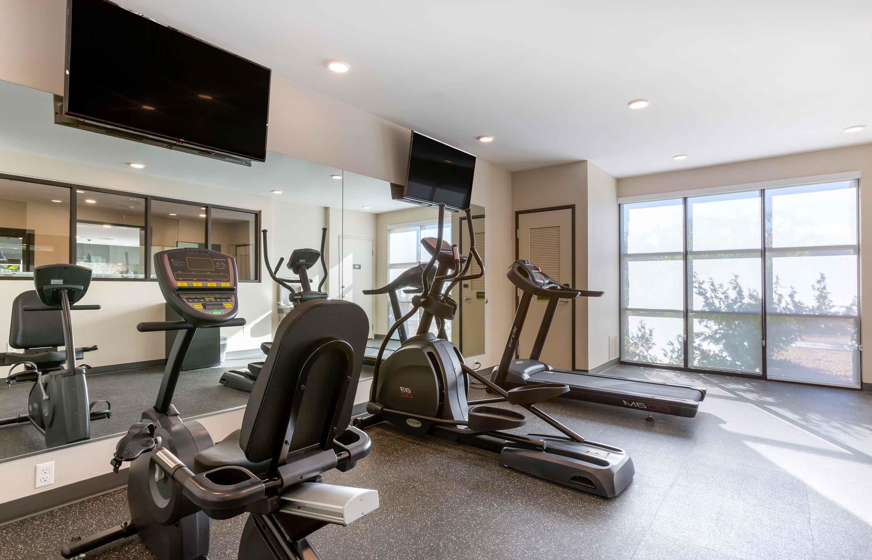 A gym with cardio machines, a TV, and large windows.