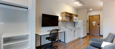 A modern apartment with a kitchenette, a flat-screen TV, a desk, and two grey armchairs.