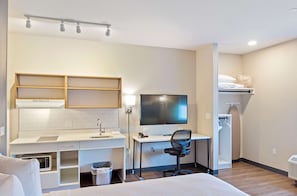 Ein Hotelzimmer mit Bett, Schreibtisch inklusive Computer, Fernseher, Mikrowelle und einer kleinen Küchenzeile.