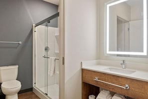 Ein modernes Badezimmer mit einer in Glas eingefassten Dusche, einem weißen Waschbecken mit Holzunterschrank und einem großen Spiegel darüber.
