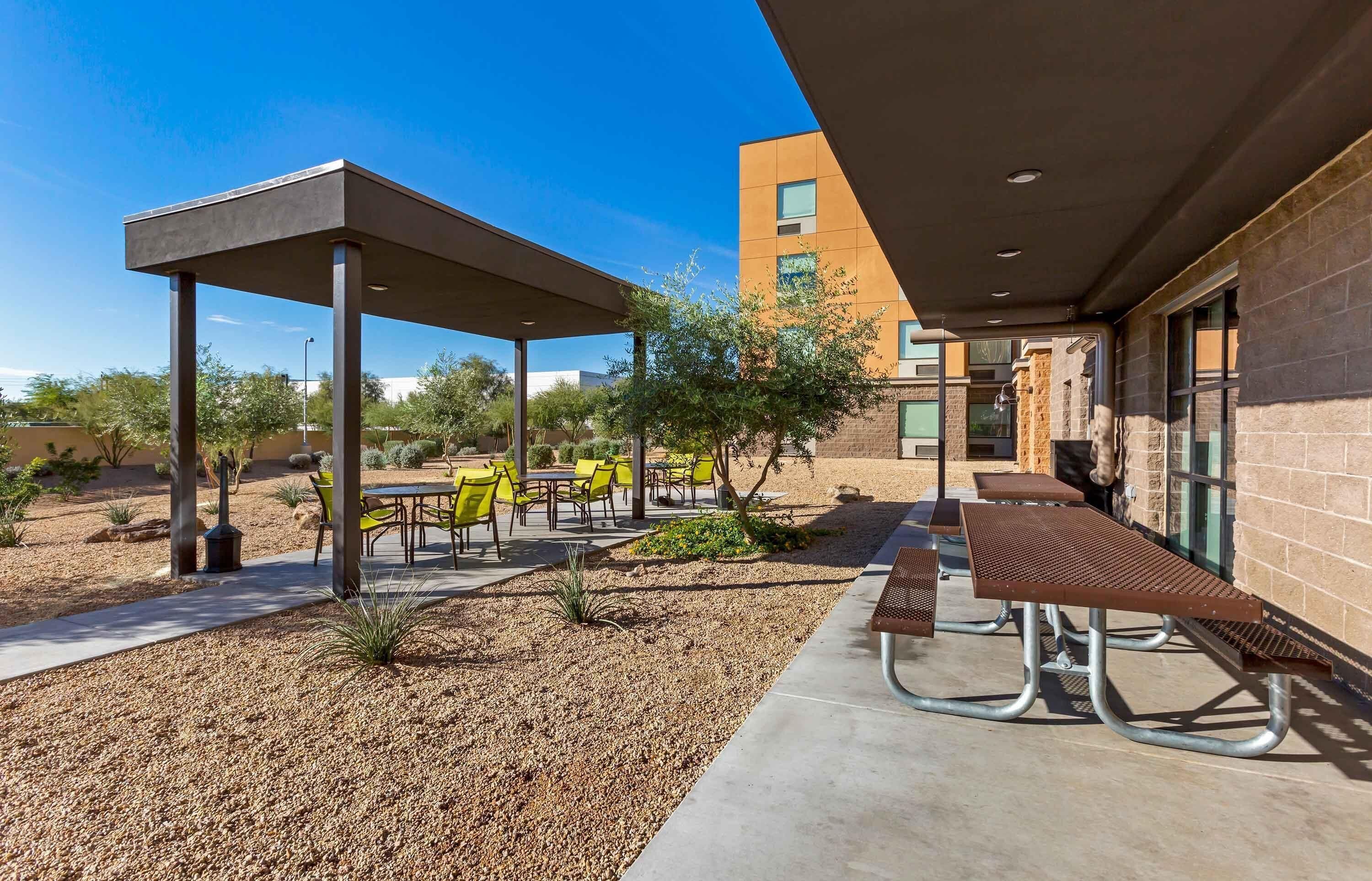 An outdoor patio area with tables and chairs, a covered seating area, and a building with a brick facade.