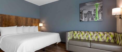 A hotel room with a bed, a sofa, a cityscape painting, and a lamp.