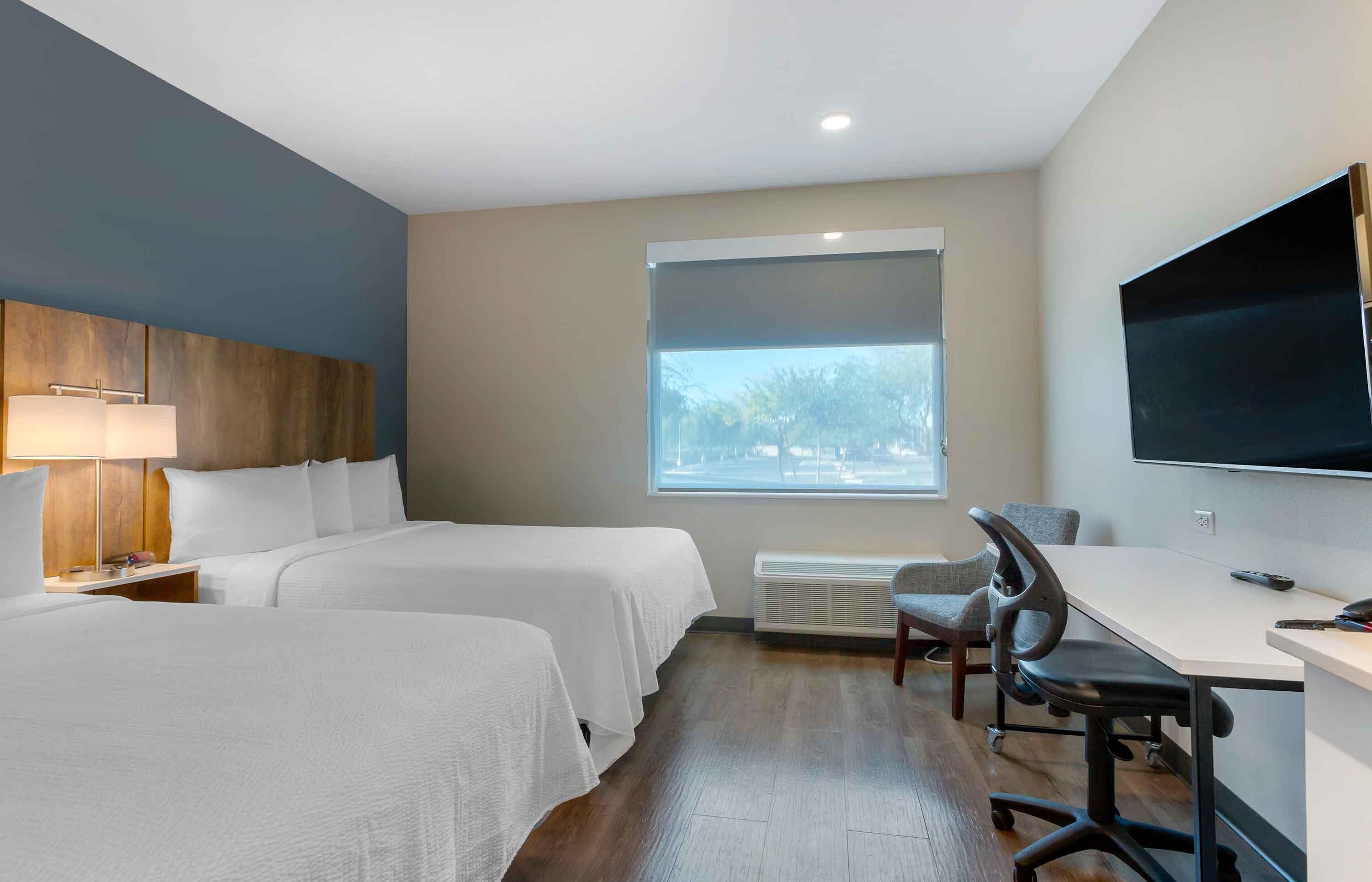 A hotel room with two beds, a desk, a chair, a TV, and a window with a view of trees.