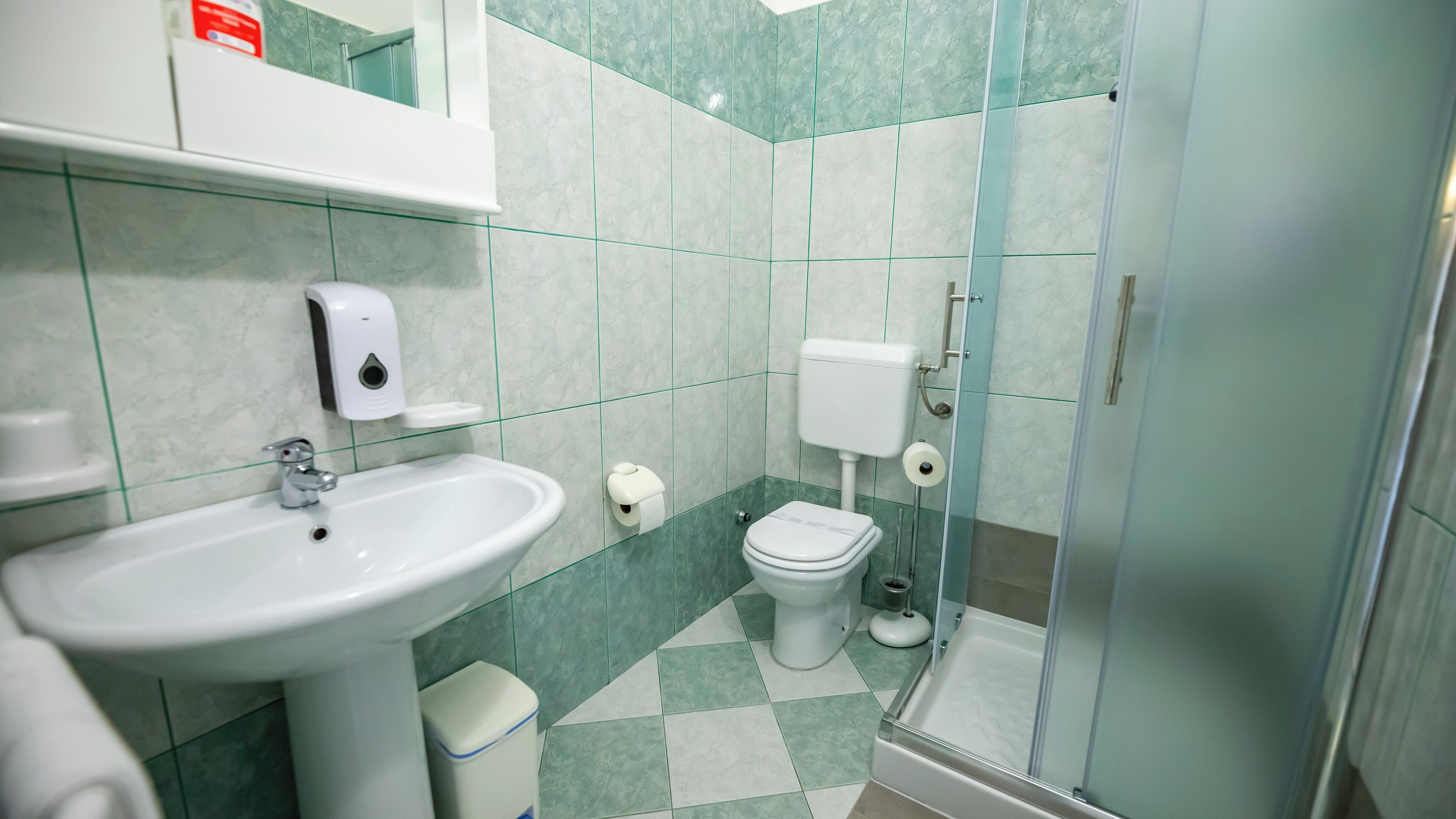Egy fürdőszoba mosdókagylóval, WC-vel és üvegfalas zuhanykabinnel.