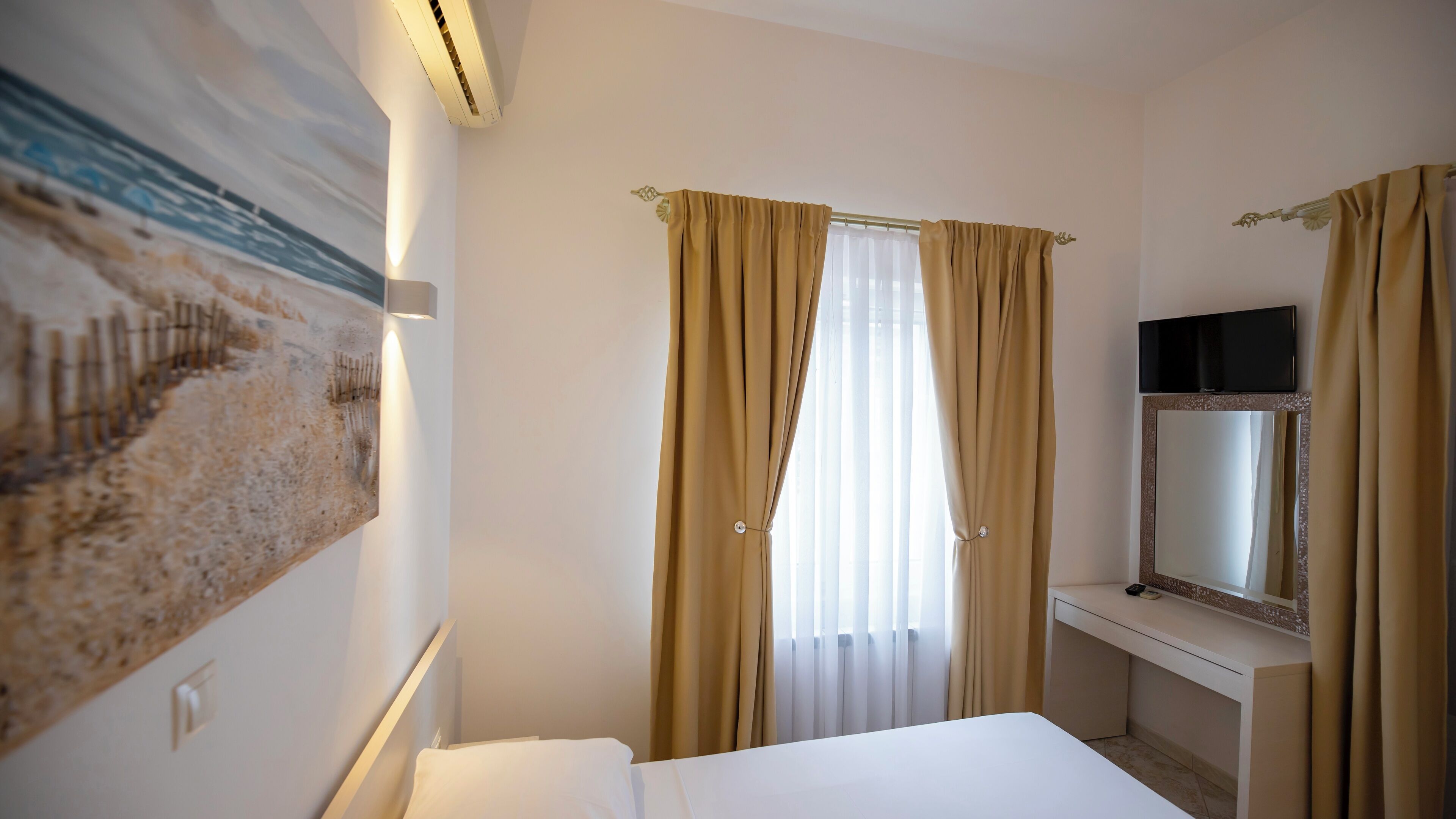 Ein Hotelzimmer mit einem Bett, einem Fernseher, einem Bild an der Wand und Vorhängen.
