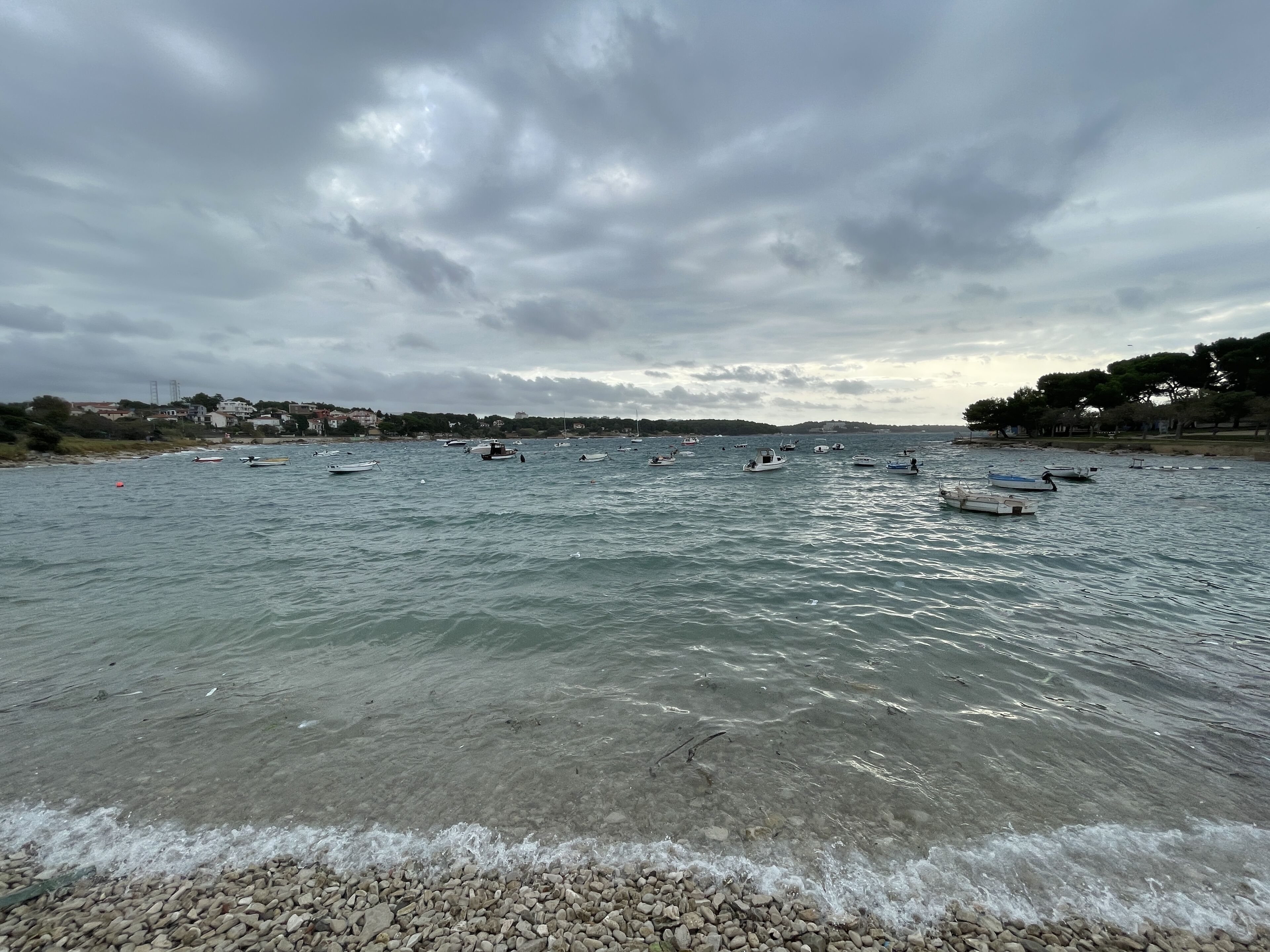 Une vue sur la côte, avec des bateaux sur l’eau et une plage de galets.