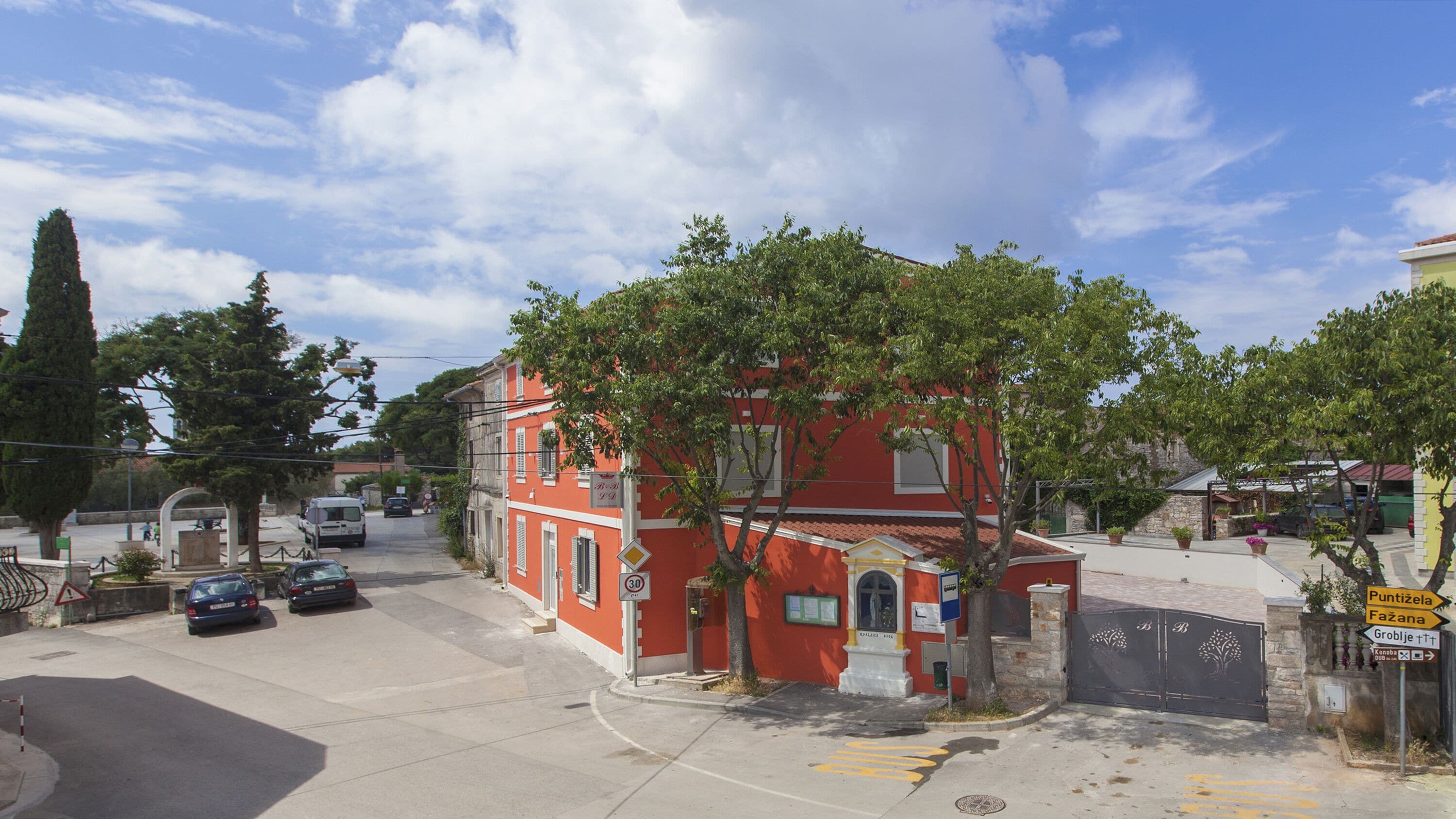 A red building with a gated entrance, a clear sky, and a few parked cars.