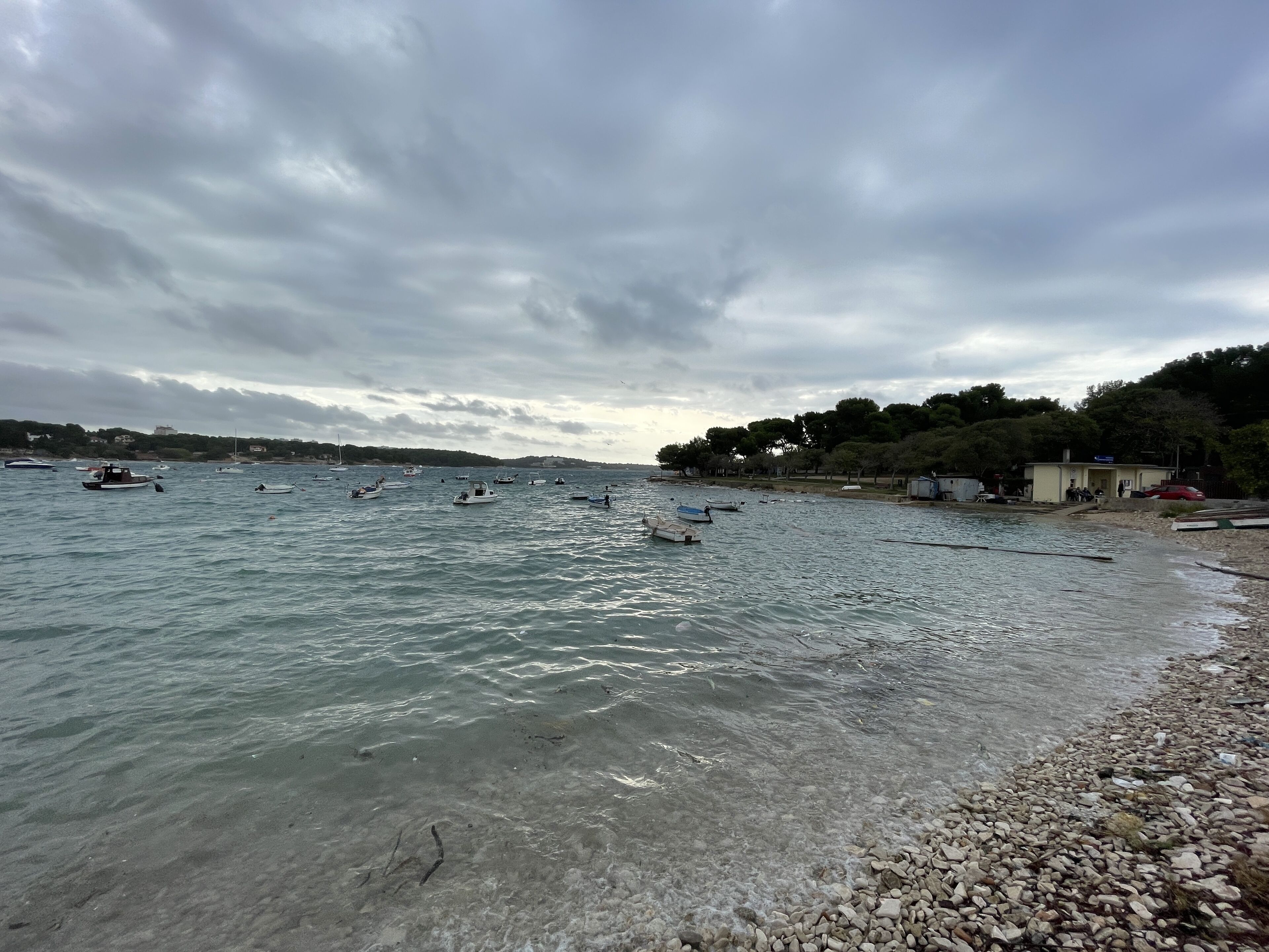 A beach with boats, pebbles, and a building with people.