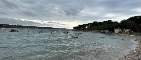 A beach with boats, pebbles, and a building with people.