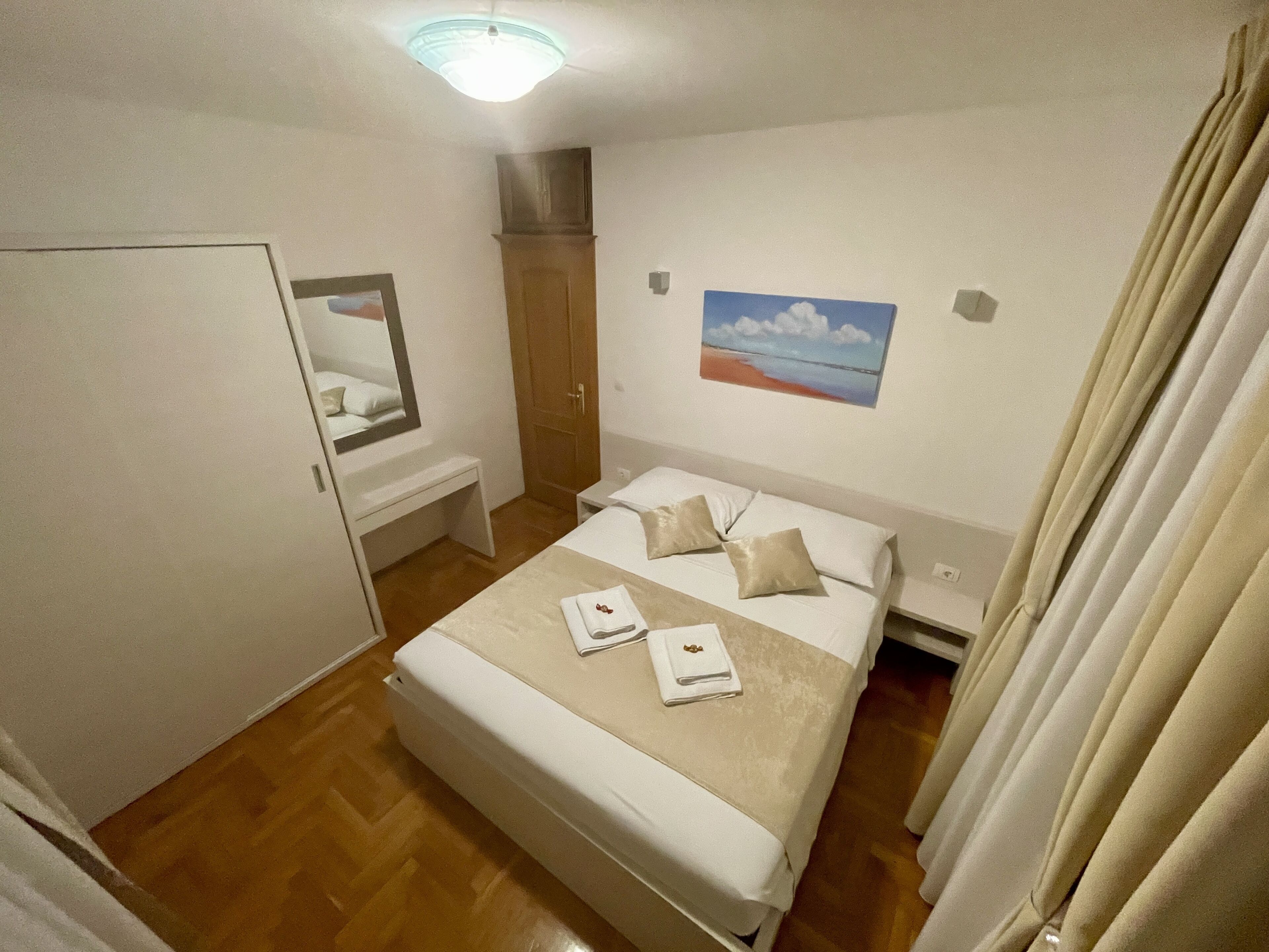 A hotel room with a bed, a bedside table, a mirror, a painting, and a door.