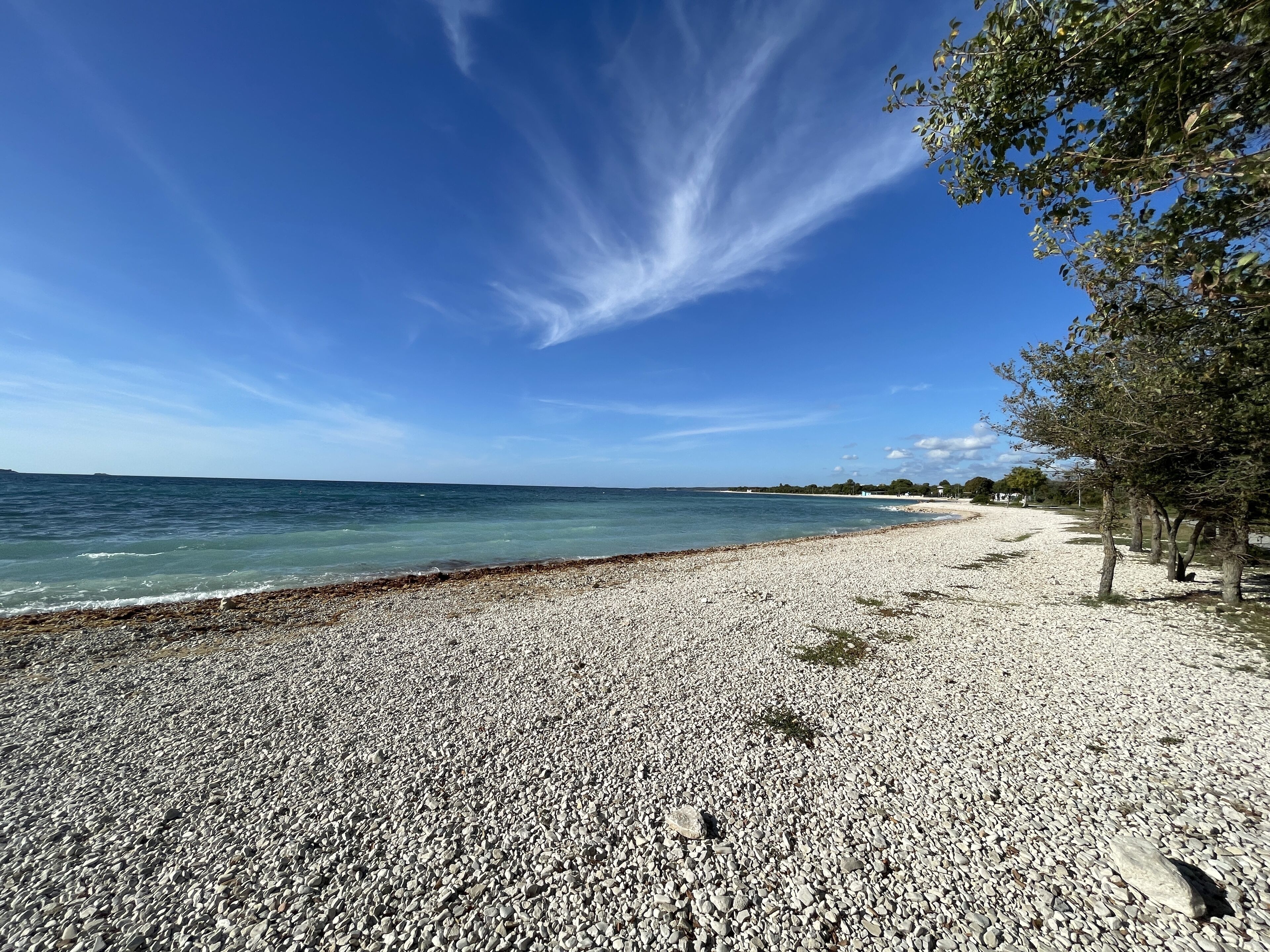 Une plage de galets, avec un ciel dégagé et une mer calme.