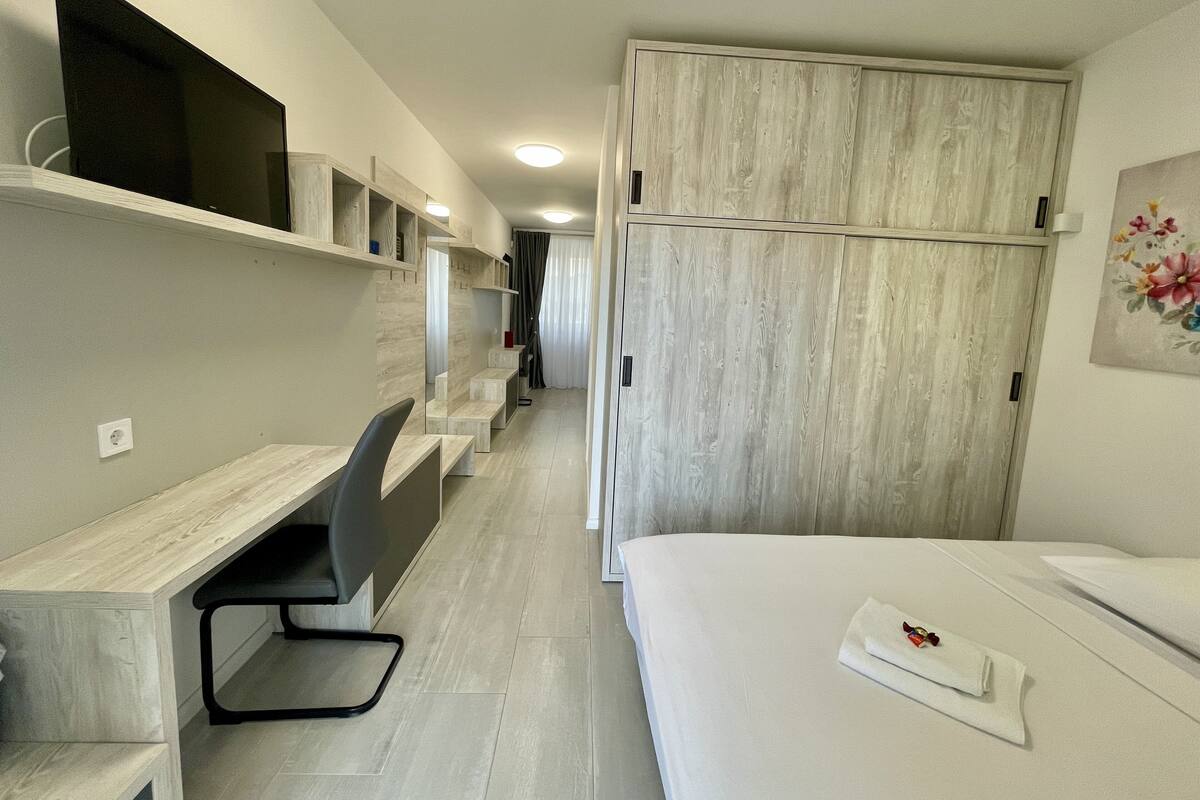 A hotel room with a bed, a desk with a chair, a wardrobe, and a television on the wall.