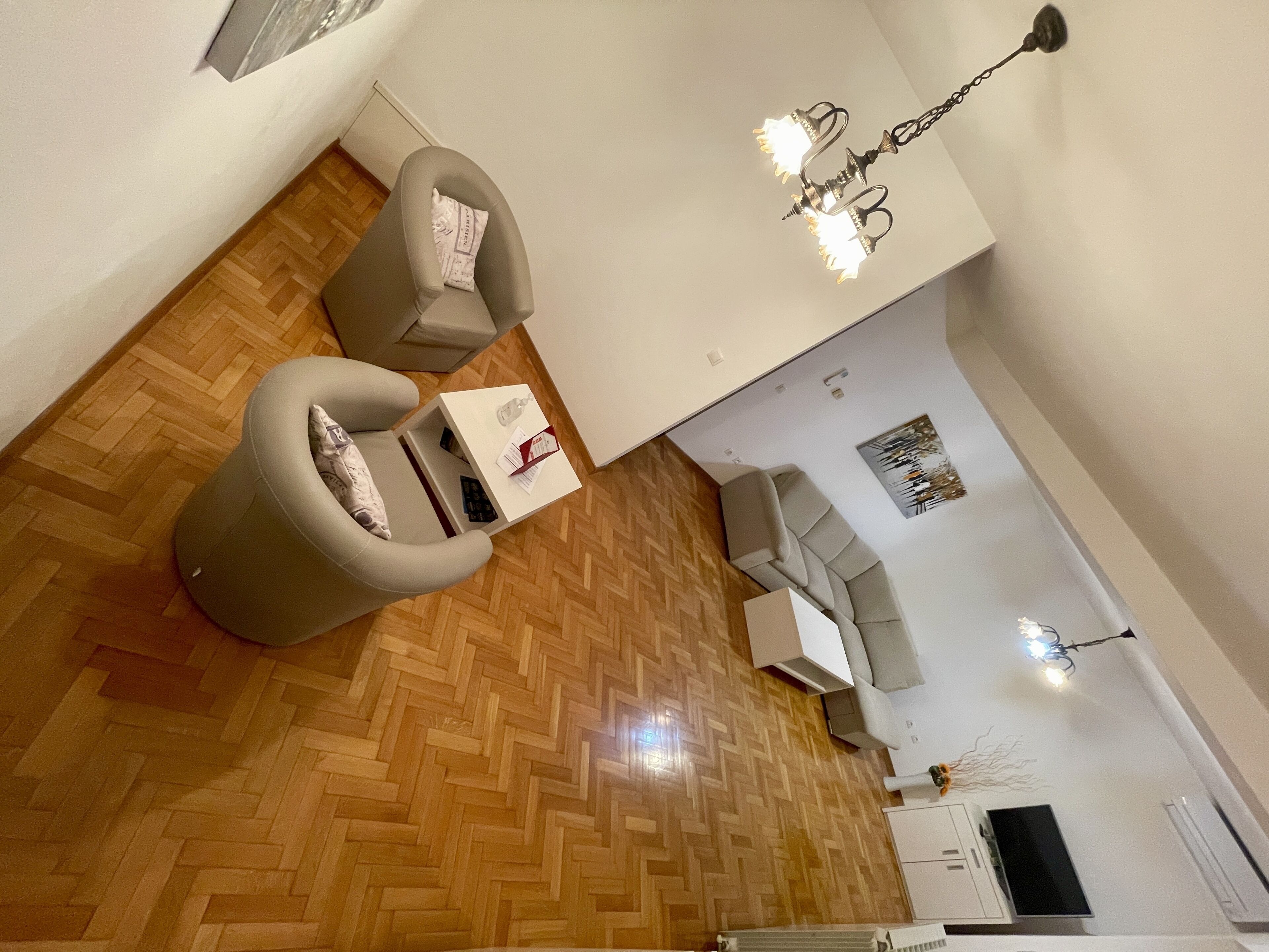 Una sala de estar moderna con piso de madera en patrón chevron, un sofá blanco, una mesa de centro blanca y una lámpara colgante.