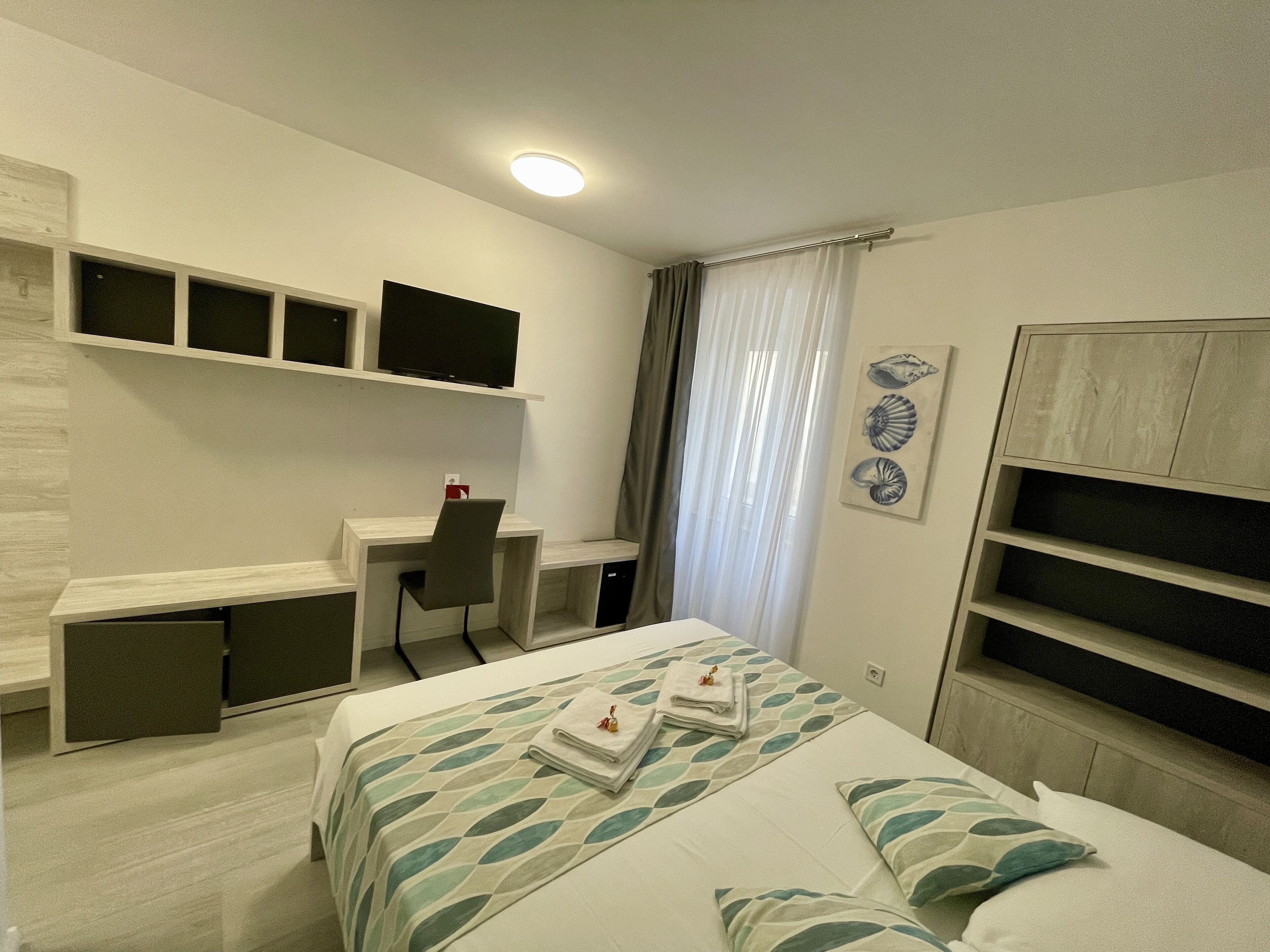 A modern bedroom with a bed, a desk, and a TV.