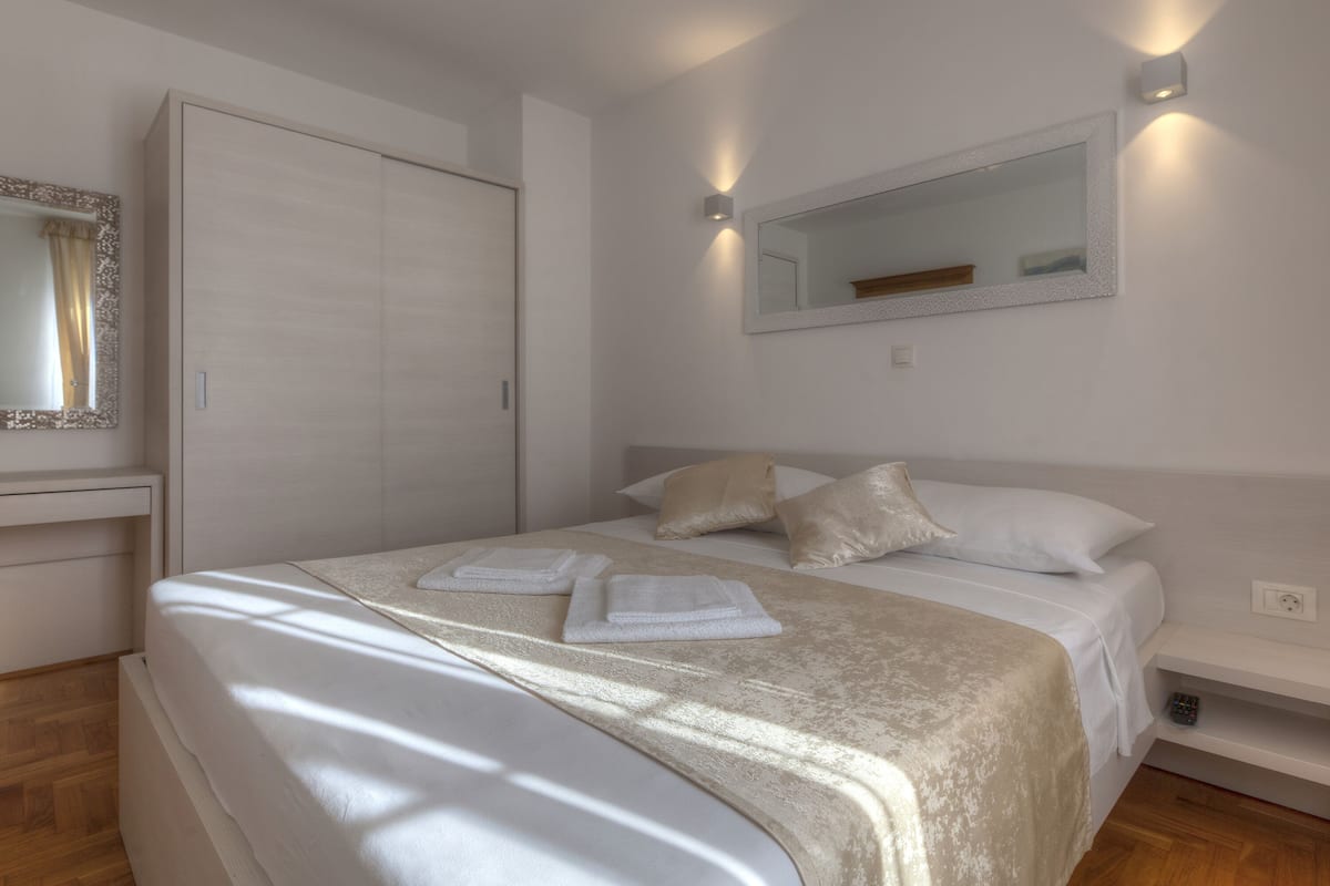 A neatly made bed with white linens and a beige throw blanket, a bedside table with a lamp, and a wardrobe with sliding doors.