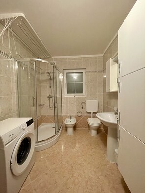 A modern bathroom with a glass-enclosed shower, a washing machine, a bidet, and a sink.