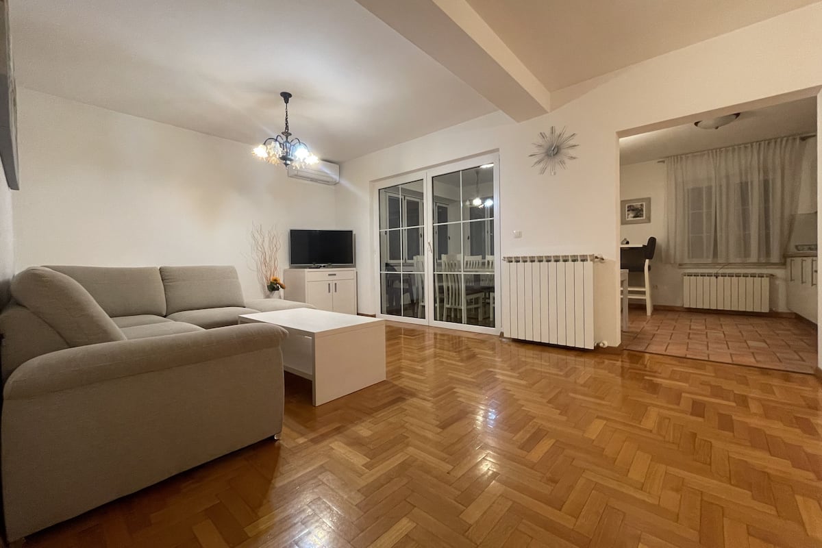 A spacious living room with a sofa, a coffee table, a TV, and a sliding glass door leading to a dining area.