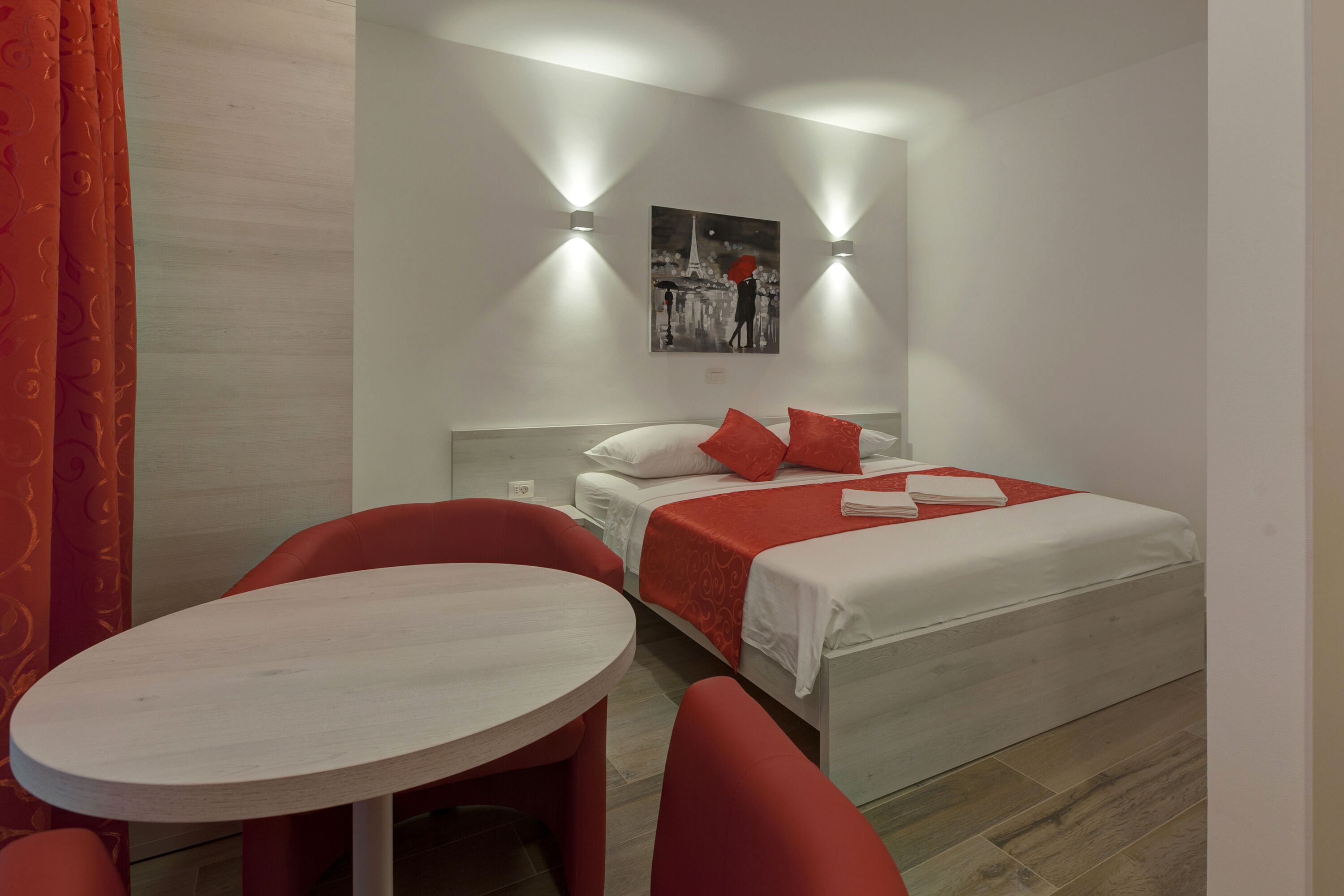 A hotel room with a bed, a round table, and two red chairs.