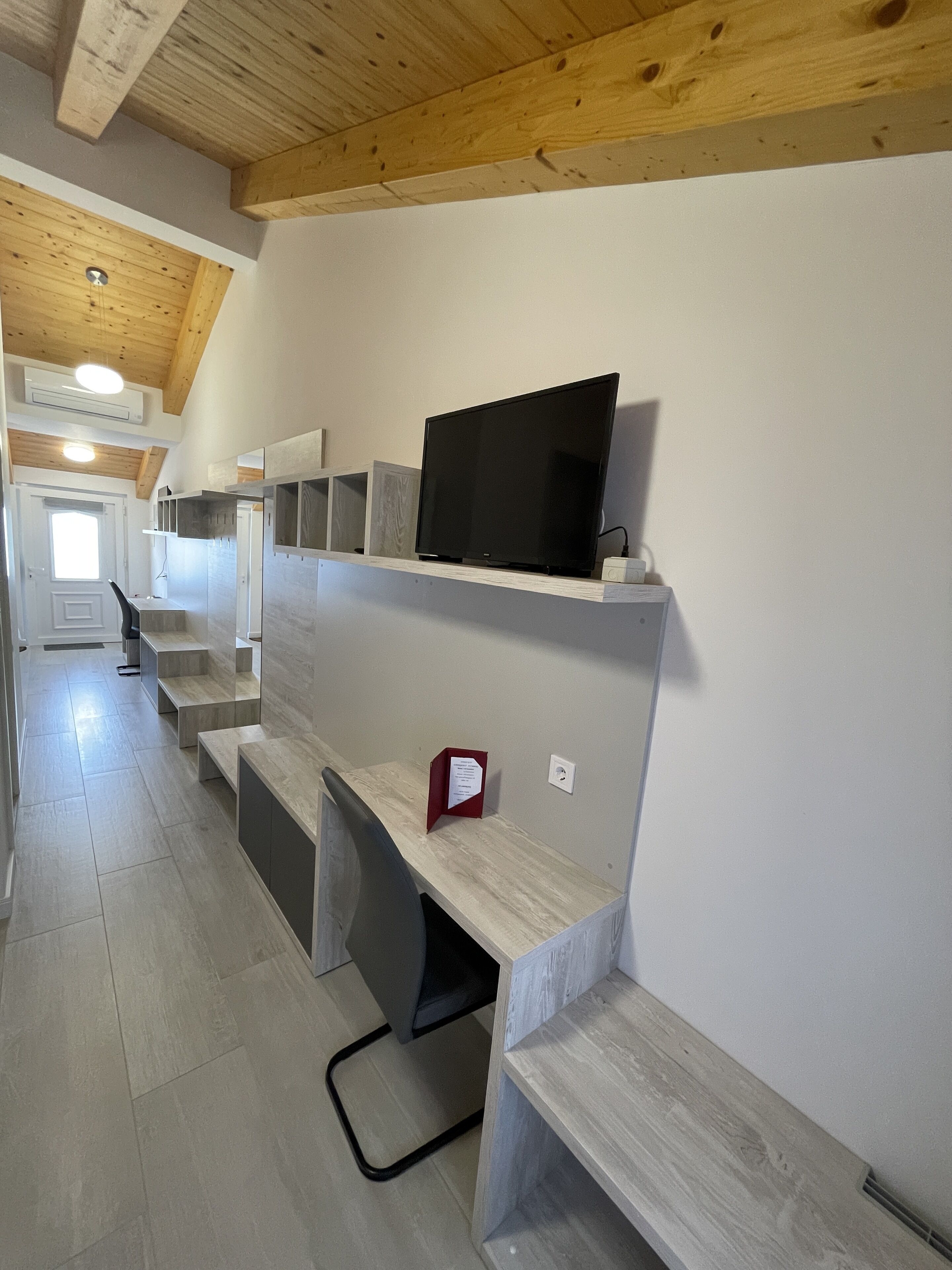 A modern interior with a wooden ceiling, built-in shelves, and a flat-screen TV.