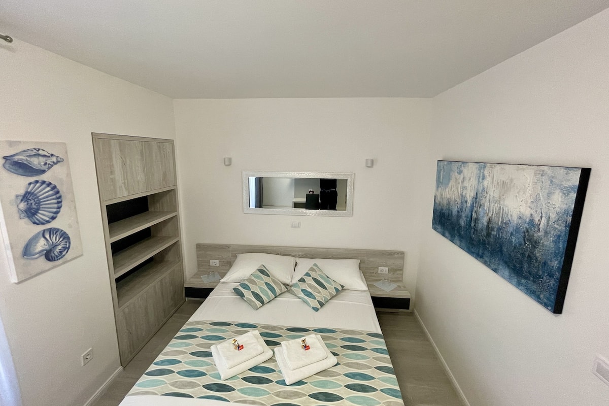 A bedroom with a bed, a wardrobe, a mirror, and artwork on the walls.