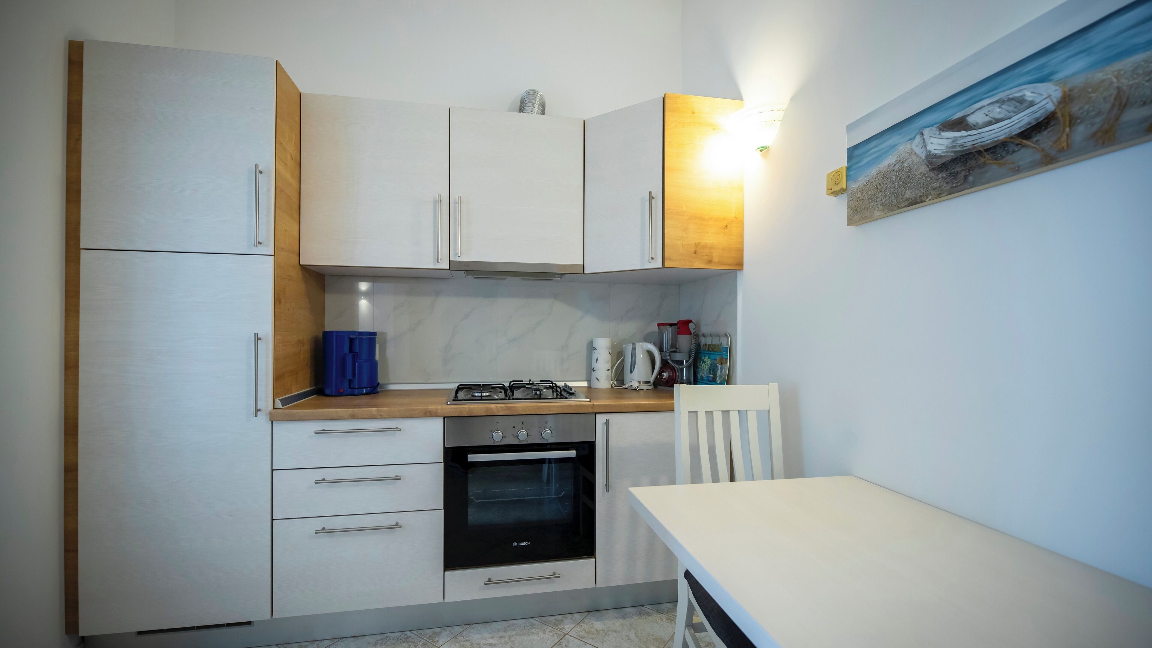A compact kitchen with white cabinets, a Bosch oven, a coffee maker, and a small dining table.