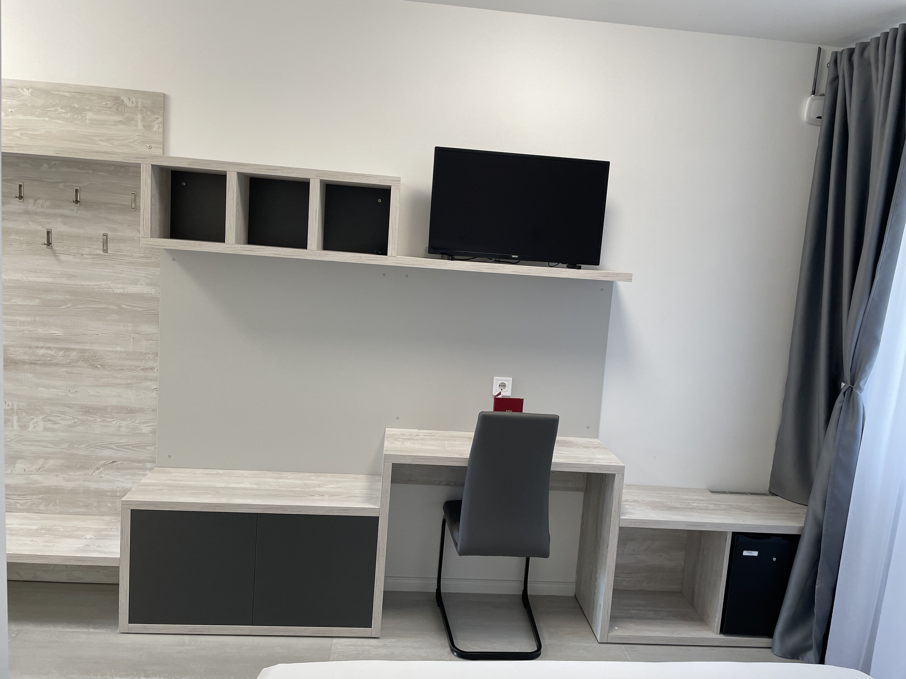 Moderni hotellihuone, jossa on työpöytä, tuoli ja seinälle asennettu litteänäyttöinen televisio.