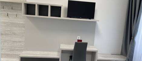 A modern hotel room with a desk, chair, and a flat-screen TV mounted on the wall.