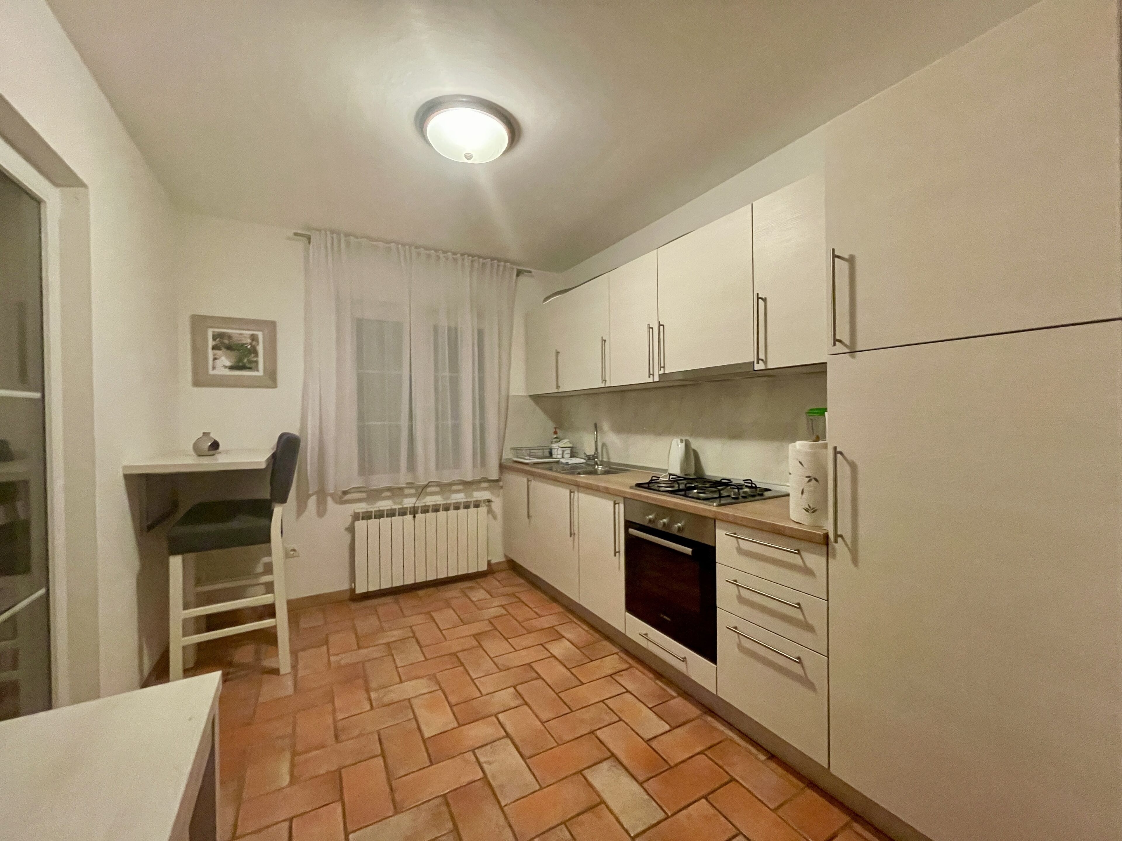 A compact kitchen with white cabinets, a gas stove, an oven, and a radiator.