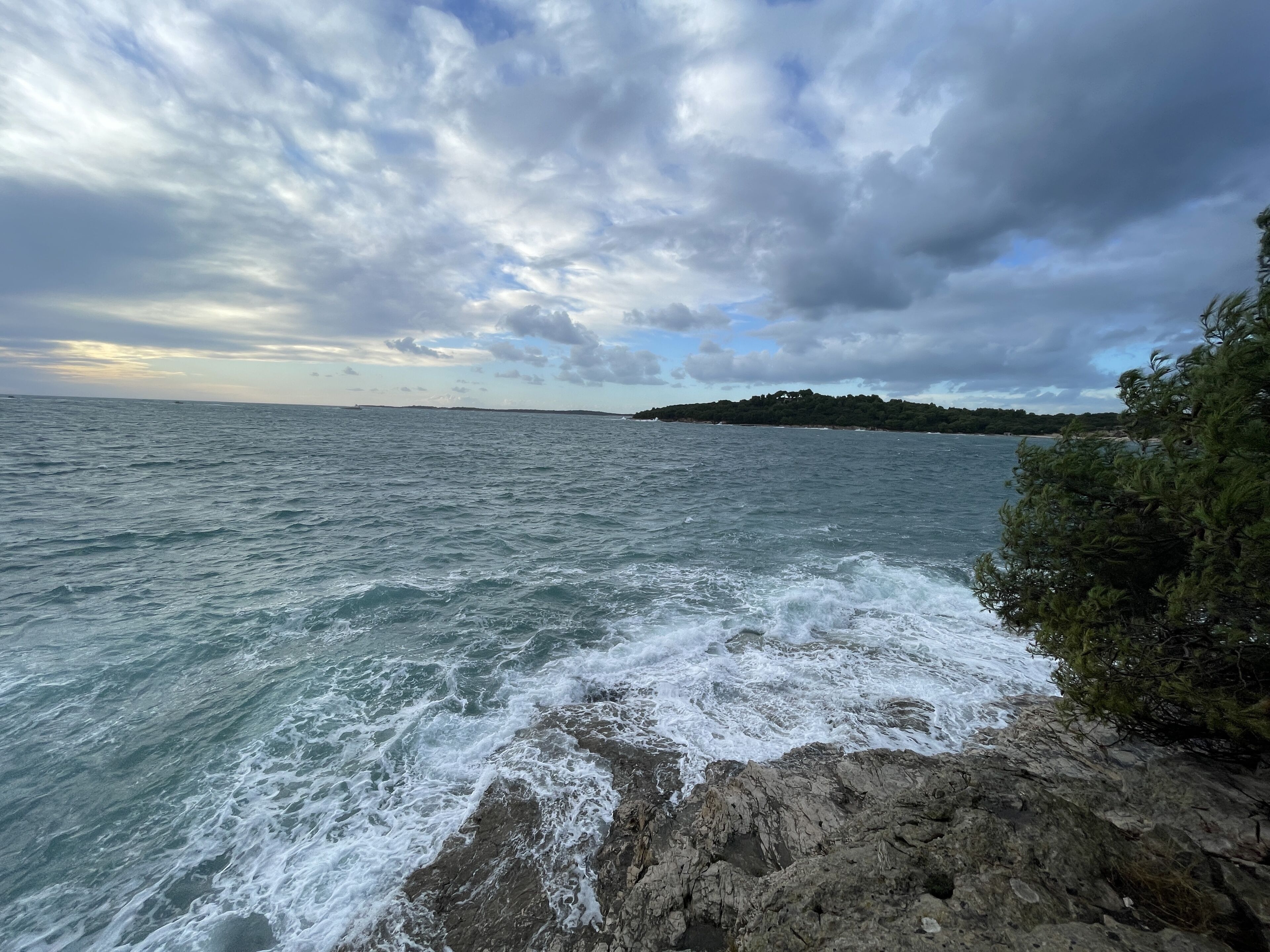 A coastal landscape with rocky terrain and a view of the sea under a cloudy sky.