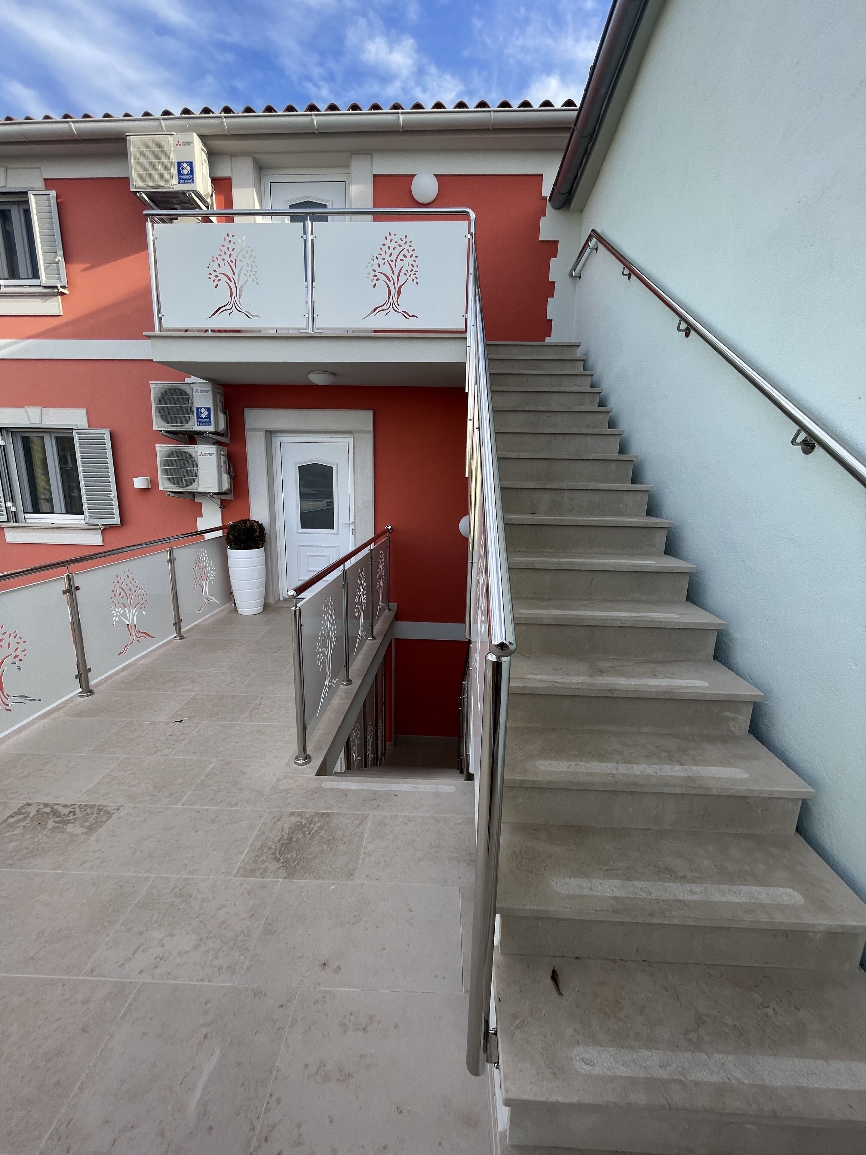 A staircase leading to a building with a red facade, air conditioning units, and a white door.