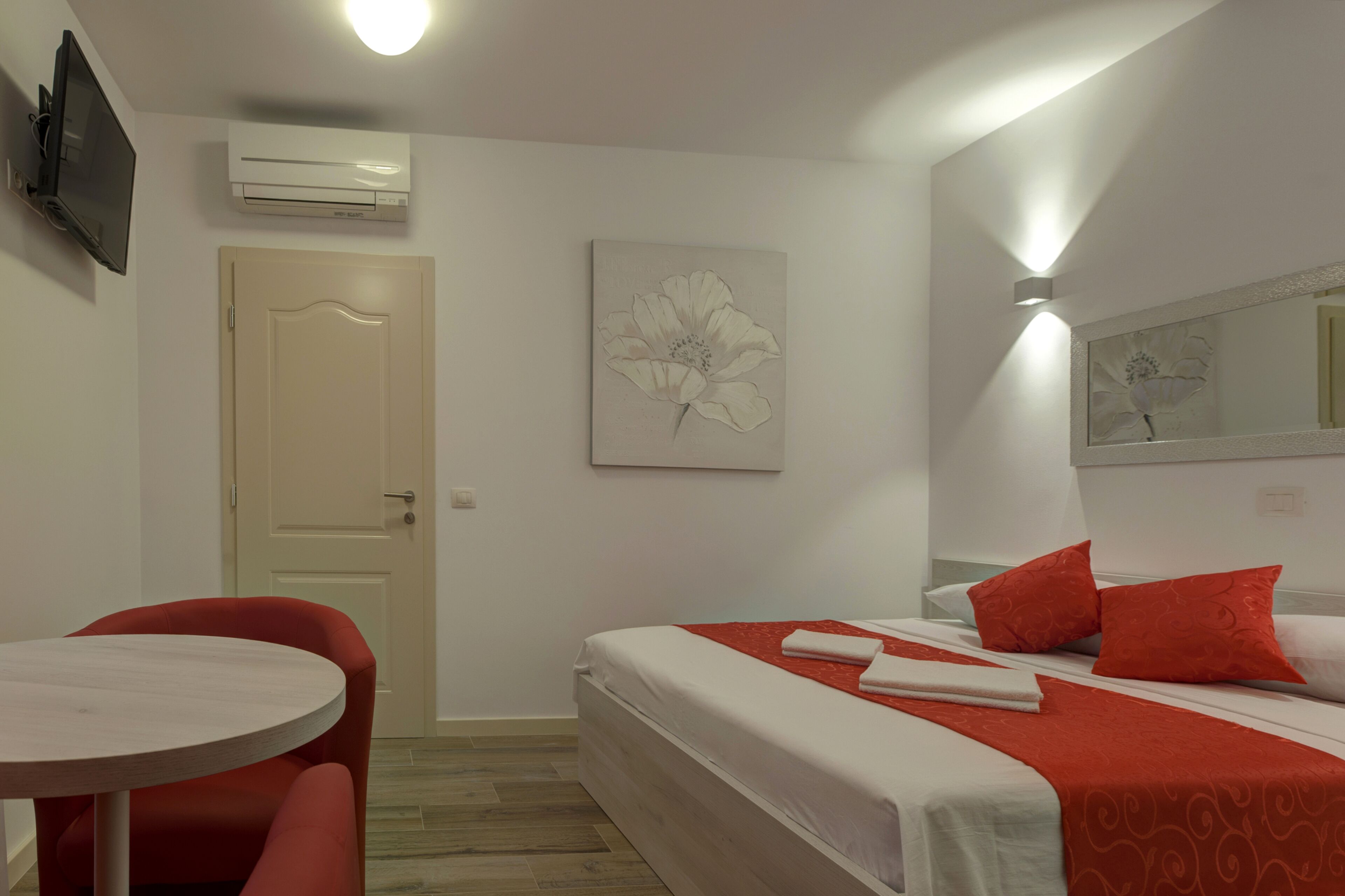 A hotel room with a bed, a chair, a table, and a wall-mounted TV.
